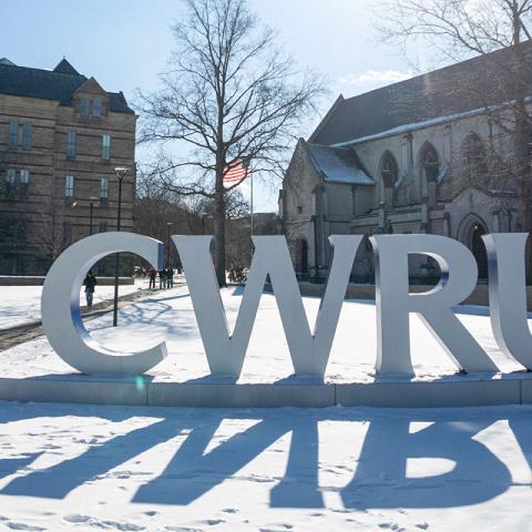 Photo of the CWRU letters on a snowy day with Adelbert Hall and Amasa Stone Chapel behind them