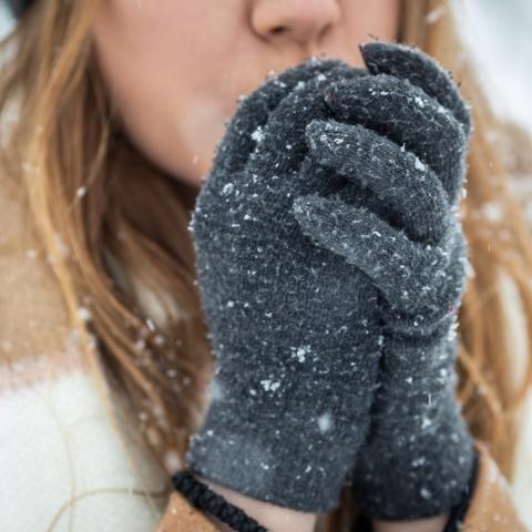 Close up of a woman blowing on her hands to warm them in the cold weather.