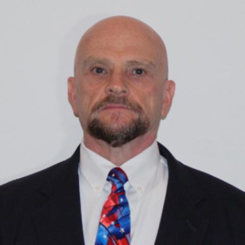 Denver Jenkins, DDS poses in front of a plain backdrop in a black suit with red and blue tie.