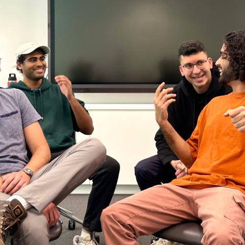 four medical students sitting in chairs, laughing with each other as they act out an improv sketch