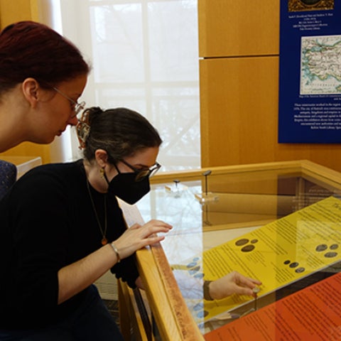 Two students assemble the ancient small coins in a glass exhibit case at Kelvin Smith Library