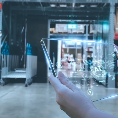 Hands hold a tablet illustrating concept of AI with a background of a warehouse