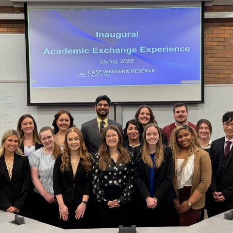 Group of students standing in front of a screen that says "Inaugural Academic Exchange Experience Spring 2026"