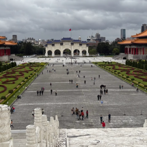 A view from the Chiang Kai Shek memorial Hallof an elaborate garden and walkway with orange-roofed buildings against a cloudy sky.