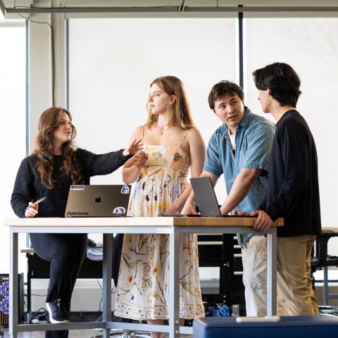 A group of Case Western Reserve University students stand in a classroom, some around a table; robotics are in the corner