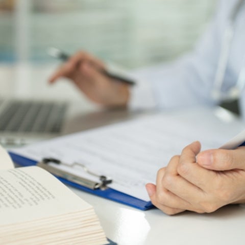 An unidentified person wearing a stethoscope writes in a book