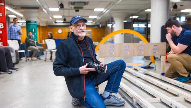 Larry Sears kneels, smiling, holding a remote control with tracks in a space at think[box]. 