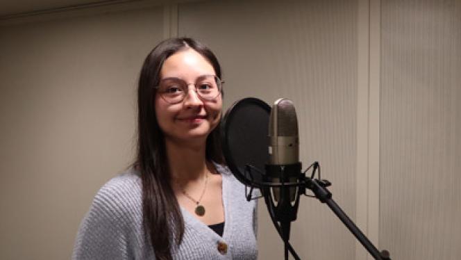 A woman stands next to a microphone in a double-walled, sound-isolated booth
