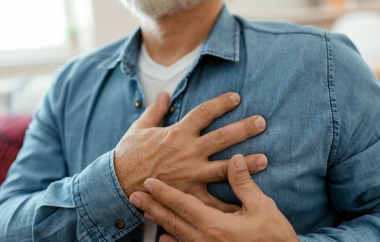 Close up photo of a man clutching his chest over his heart with both hands