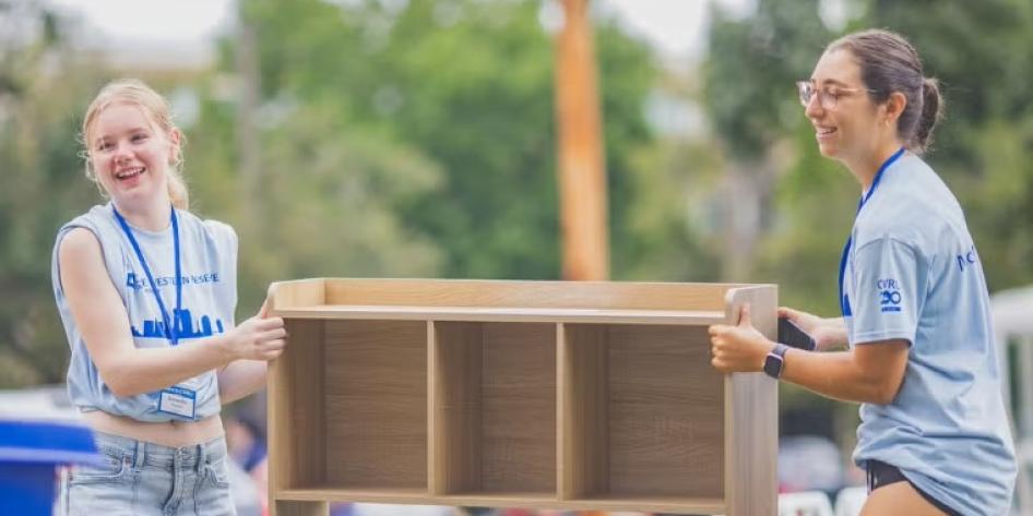 Two CWRU student move-in helpers carry an organization cube to a new student's room.