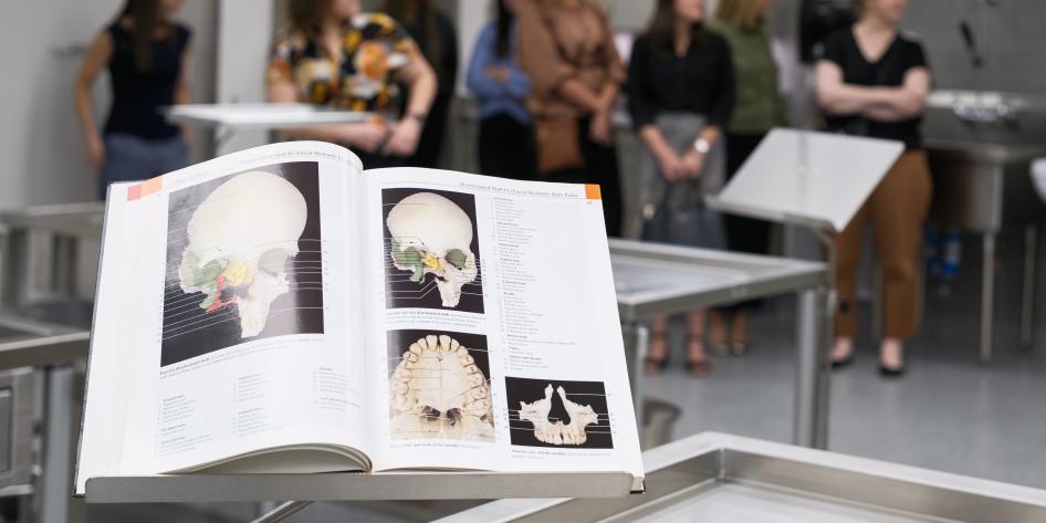 Anatomy textbook with pictures of skulls displayed on a bookstand in a room full of people