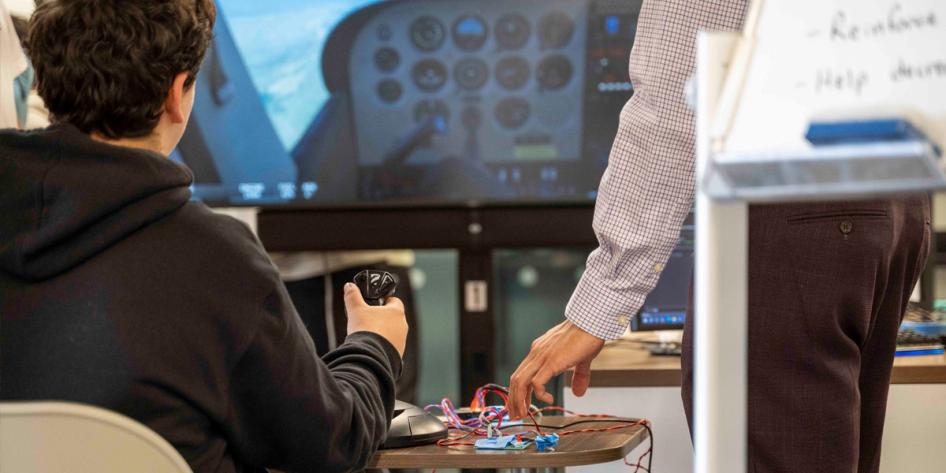 Photo of a student with their hand on a controller looking at a screen simulating airplane flight