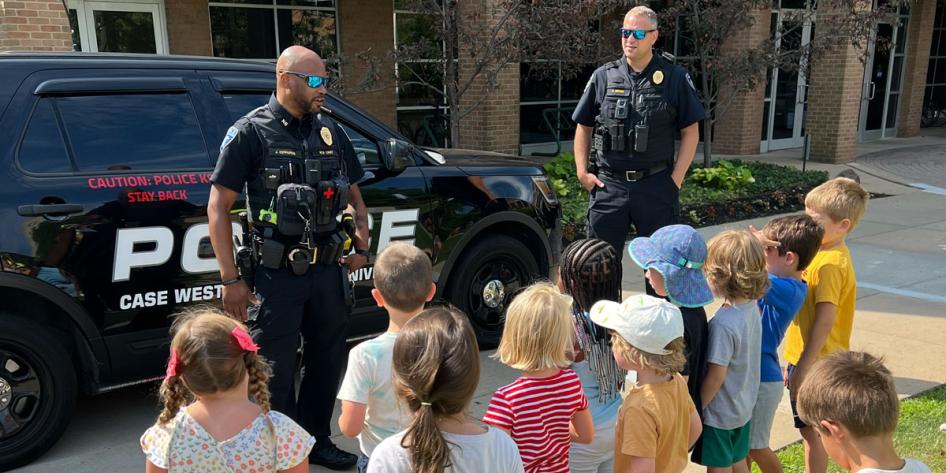 Photo of two CWRU police officers talking to children in front of a police vehicle