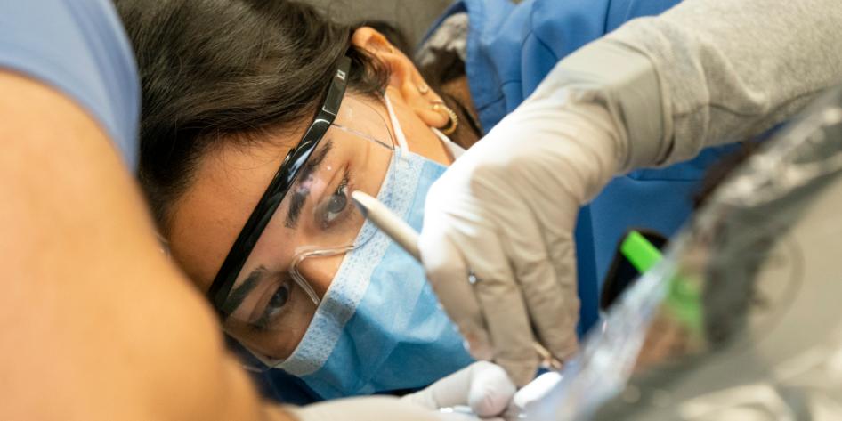 Closeup of a dental student in glasses and a mask working on a patient.
