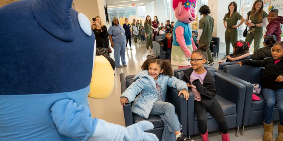 Children smile in the dental school waiting room as they are greeted by Bluey and Troll mascots