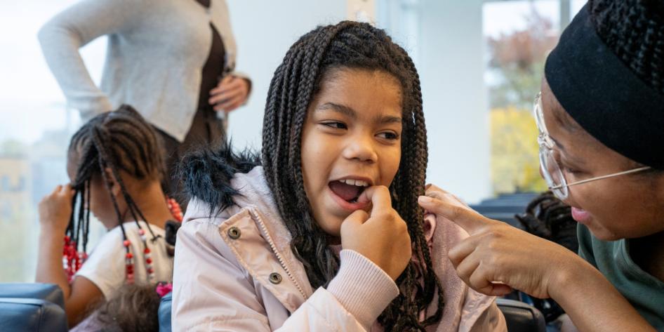 A second-grade student sits in the waiting room and points in her mouth to show a dental student where she lost a tooth.
