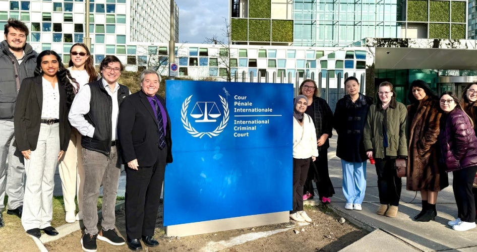Participants of the “Spring Break in The Hague” program gather around a sign at the International Criminal Court. 
