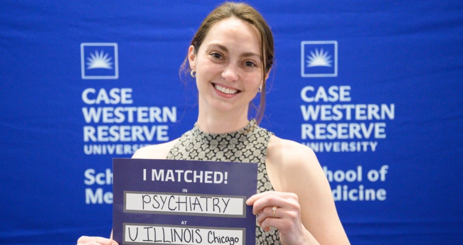 student holding a sign that says "I matched in psychiatry at U Illinois Chicago" in front of a blue CWRU School of Medicine backdrop
