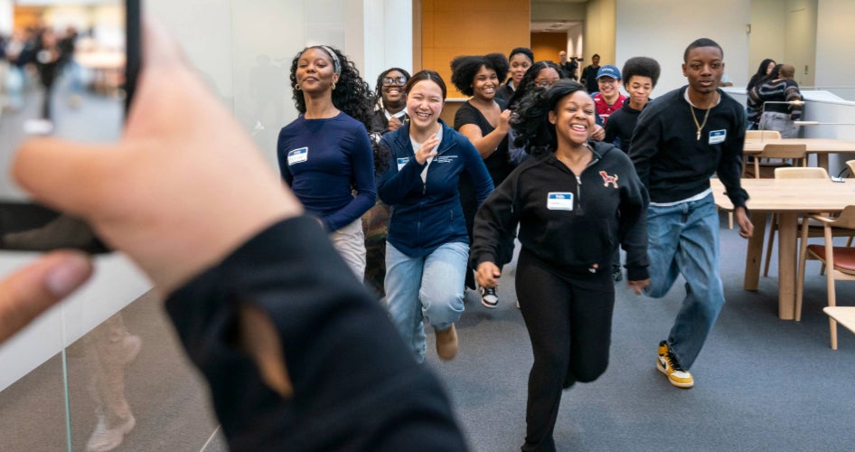 A group of students runs down a hall while someone photographs them.