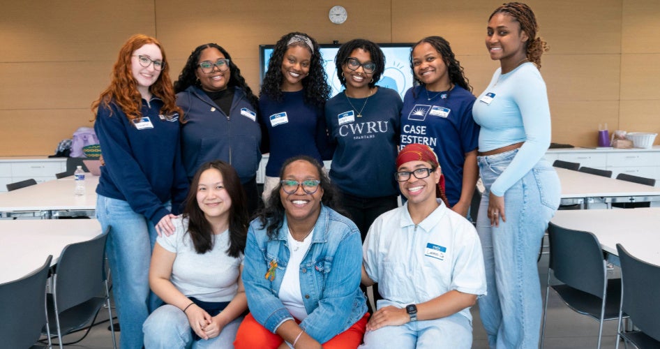 A group of nursing students in blue sweatshirts poses for a group photo with a brown wall behind them.