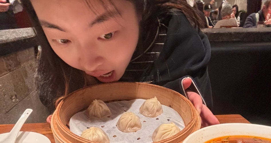 A woman leans over a plate of food with her mouth open.