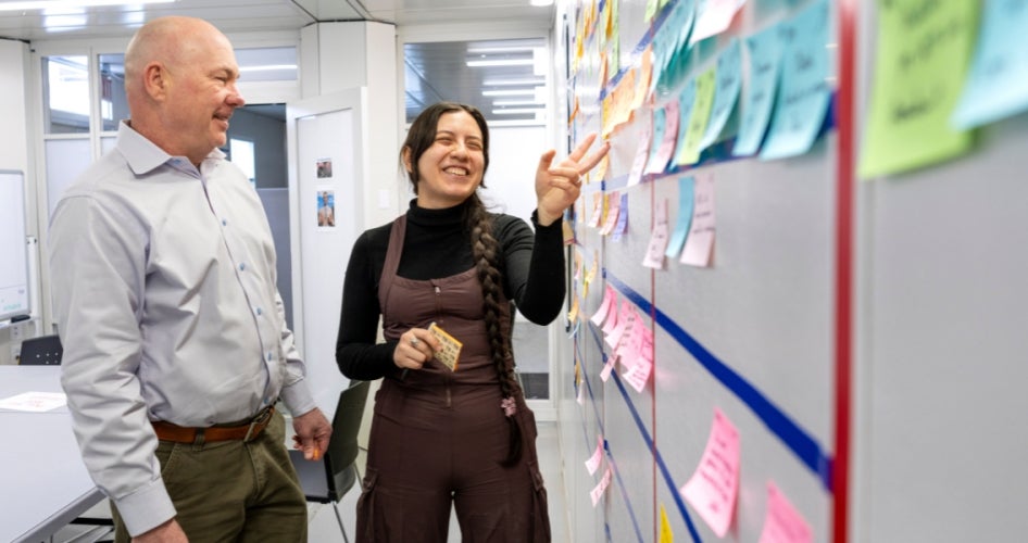 Jack Kellogg (pictured left) and Abigail Mondragon discuss progress of the Interdisciplinary Science and Engineering Building project at a Kanban board. Photography by Nancy Andrews. 