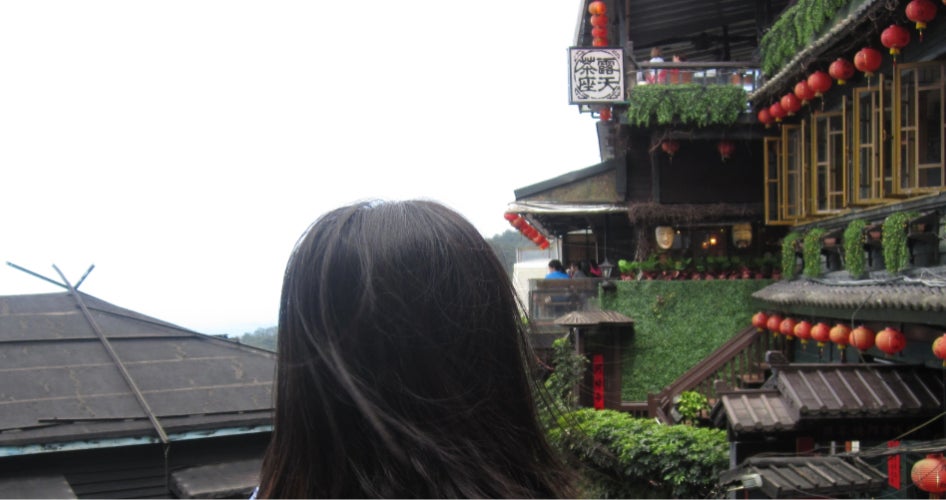 The back of a woman's head in front of a red temple and grey skies.