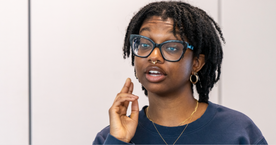 A woman in glasses and a blue sweatshirts demonstrates on her neck how to take a pulse.