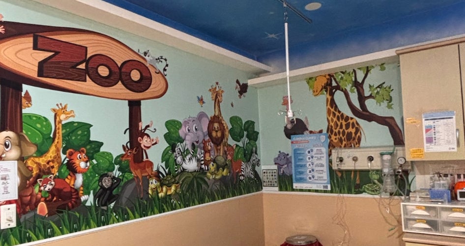 A pediatric hospital room with a large zoo mural on the wall.