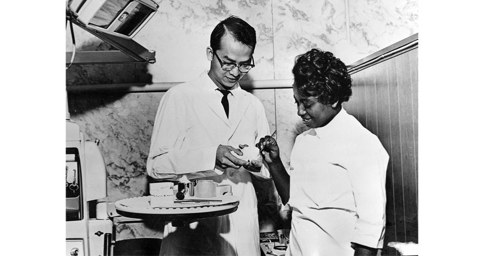 A man and a woman in lab coats are examining dental molds in a dental office. The woman smiles while observing, creating a professional and positive atmosphere.