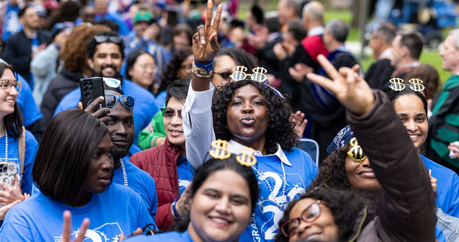 Students wearing blue 2026 graduate shirts smile and pose as they crowd together on campus walkways for clap out