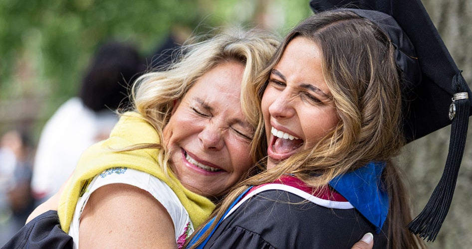 Close up photo of a young woman in her cap and gown hugging a family member