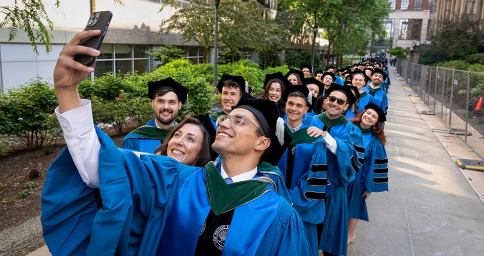 A graduate from the School of Medicine holds his phone up to take a photo of the procession to the ceremony