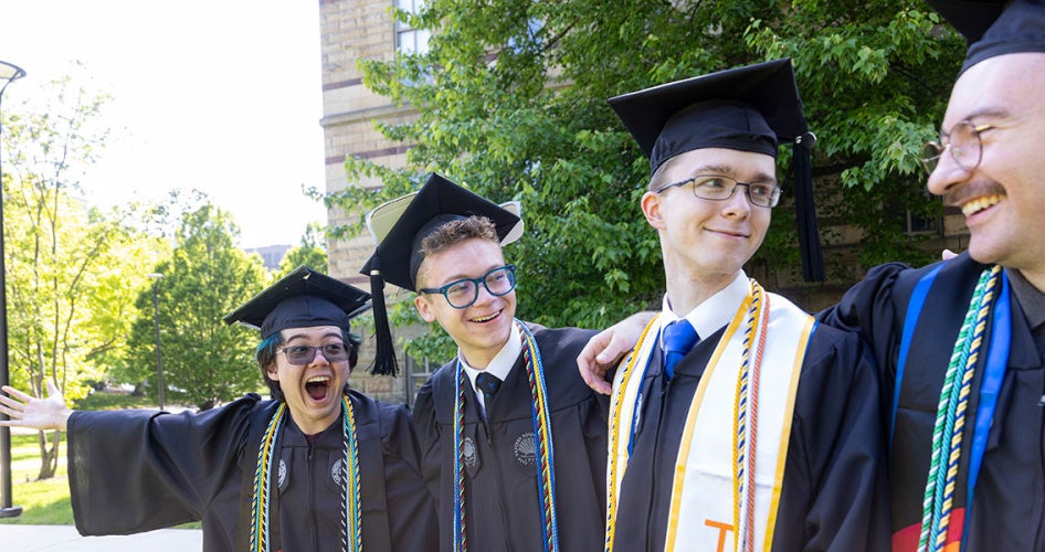 Four graduates in their caps and gowns pose for a photo with their arms around one another