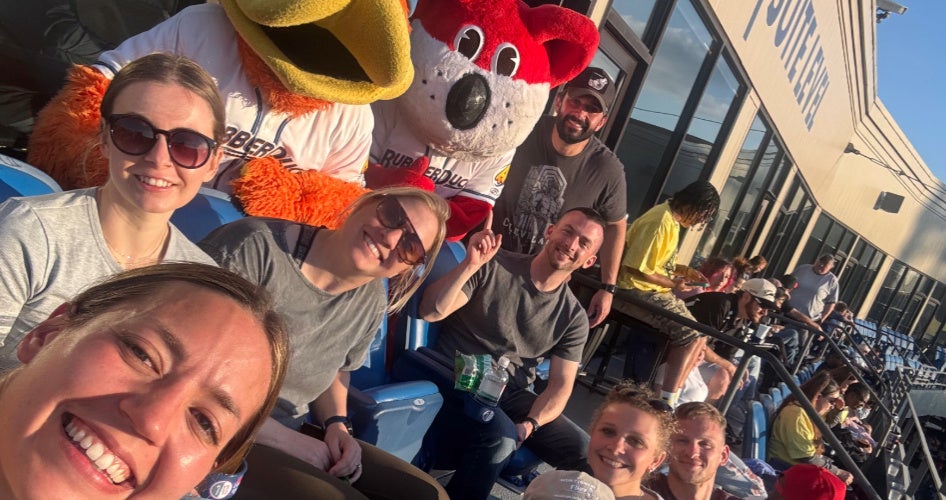 A group of people smiles at the camera at a baseball game with mascots behind them.