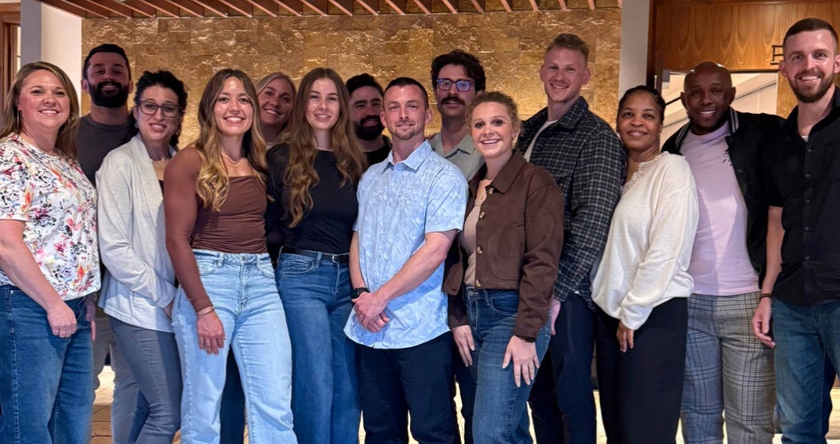 A group of people poses in front of a wooden wall.