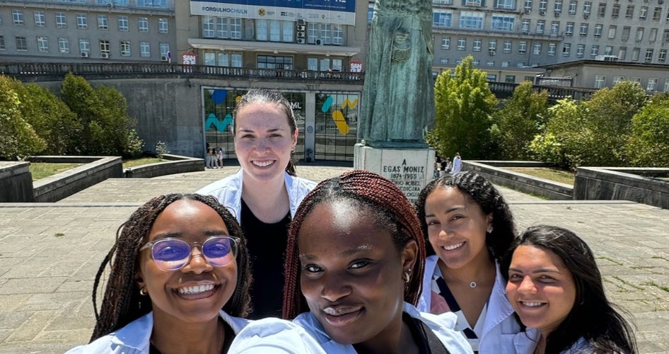 A group of women smile in a courtyard in front of a hospital.