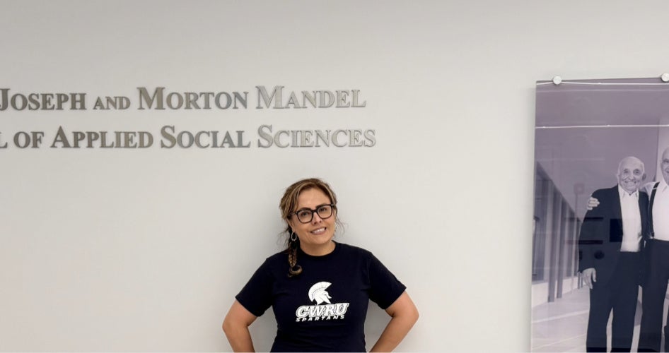 Edith Cabrera in blue CWRU shirt in front of a Mandel School plaque