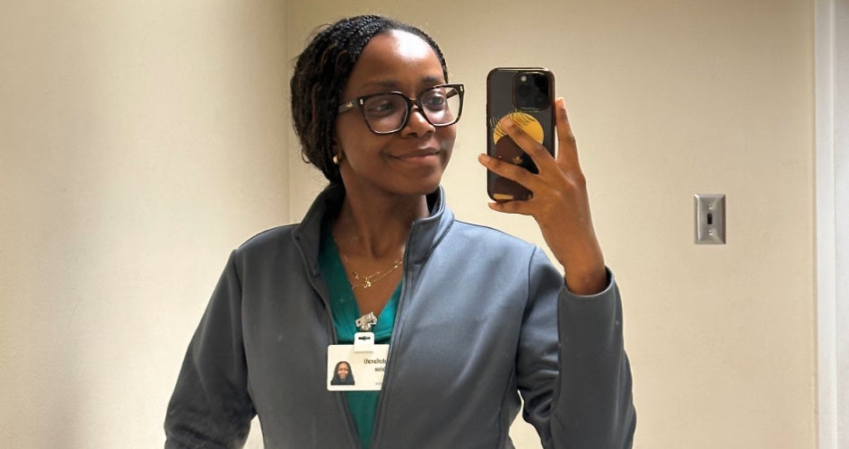 Adebise holds a phone to take a selfie while wearing blue scrubs.