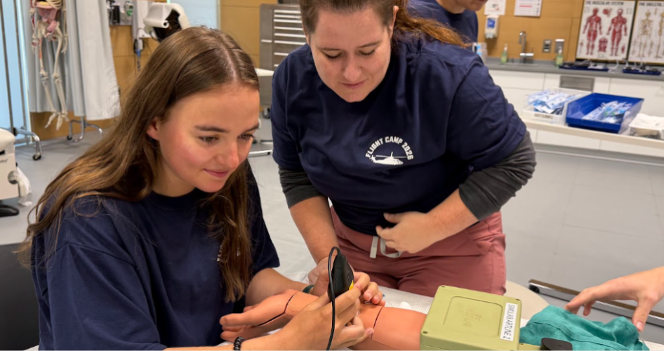 A student in a blue shirt practices an ultrasound on a medical mannequin's wrist.