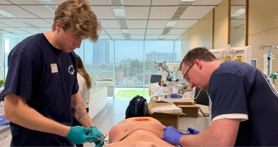 A student in a blue shirt works on a medical mannequin with an instructor.