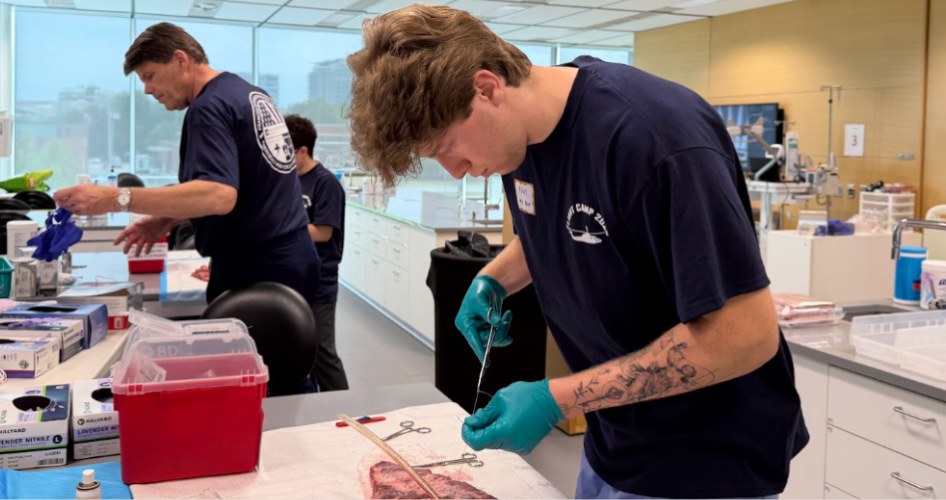 A student practives sutures on a piece of meat.