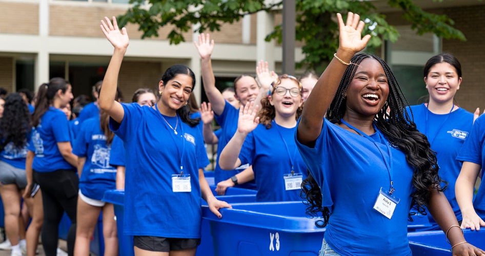 A line of orientation leaders wearing CWRU blue shirts wave to arriving first year students during move-in