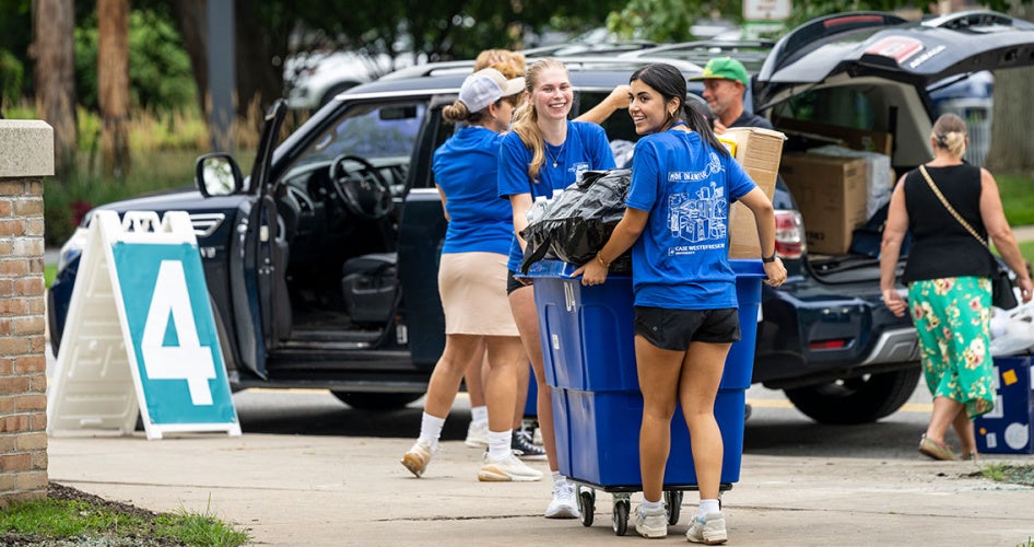 Orientation leaders and volunteers load up a cart with an arriving student's belongings during move-in
