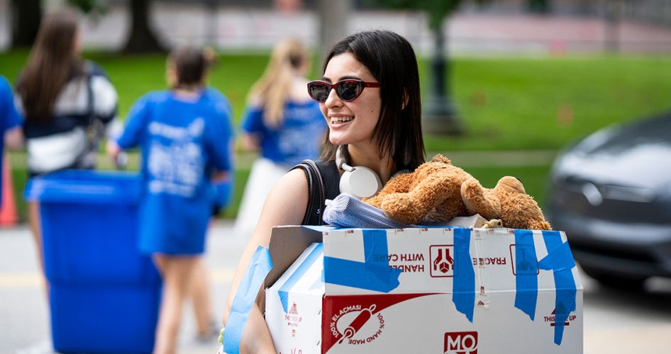 A new CWRU student carries a box of her belongings during move-in