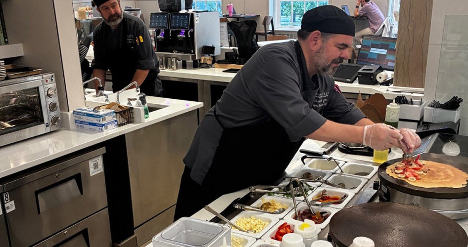 An employee sprinkles toppings onto a crepe being made on a hot plate