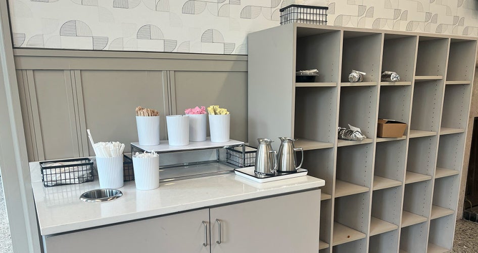 A counter with self-service coffee cups, lids and sugar next to organizer cubes where orders are placed