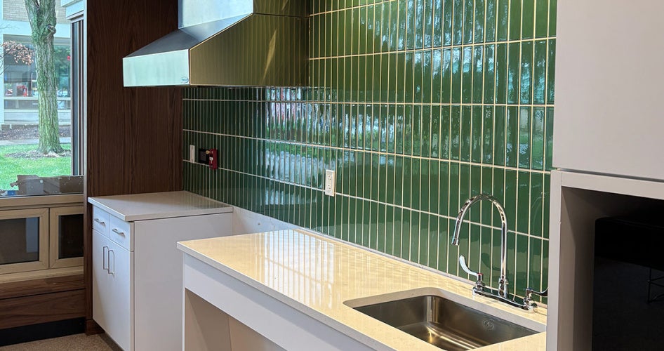 Photo of a green tiled wall contrasted with white counters and cabinets in a kitchen area of Tyler House