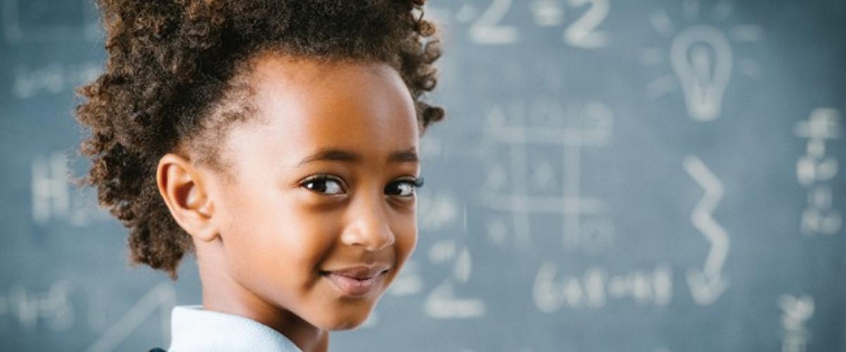 Girl looks back and smiles in front of a chalkboard with math problems on it