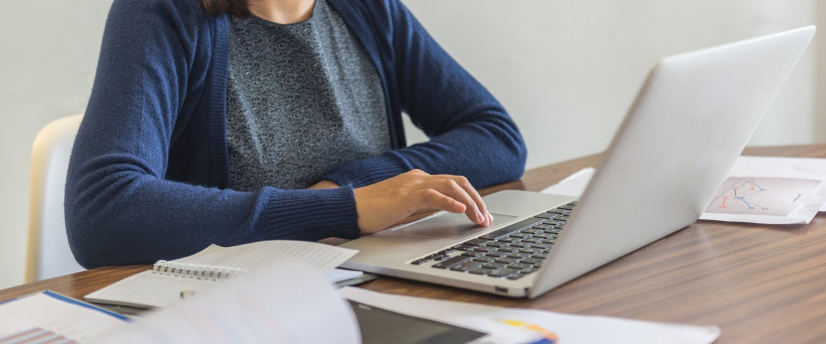 Woman typing on laptop surrounded by papers